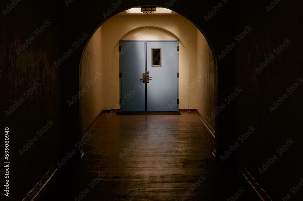 Blue door illuminated at the end of long dark hallway