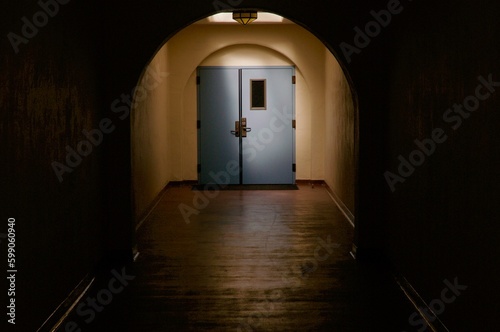 Blue door illuminated at the end of long dark hallway