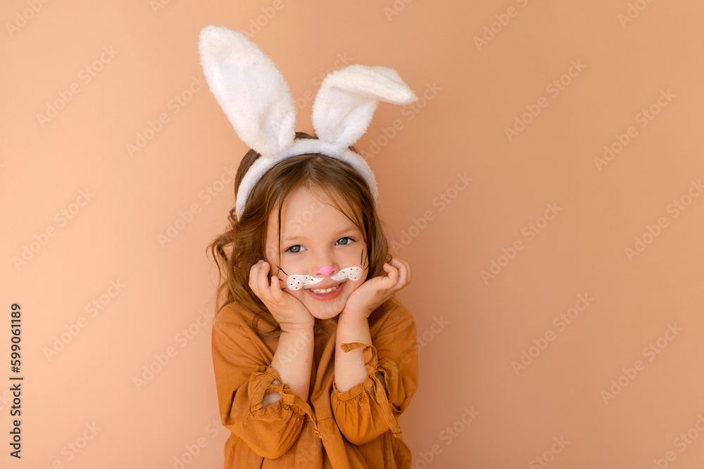 A sweet, pleasant little girl dressed up in an Easter bunny costume looks in surprise at the camera with big blue eyes, pressing the boats to her cheeks.