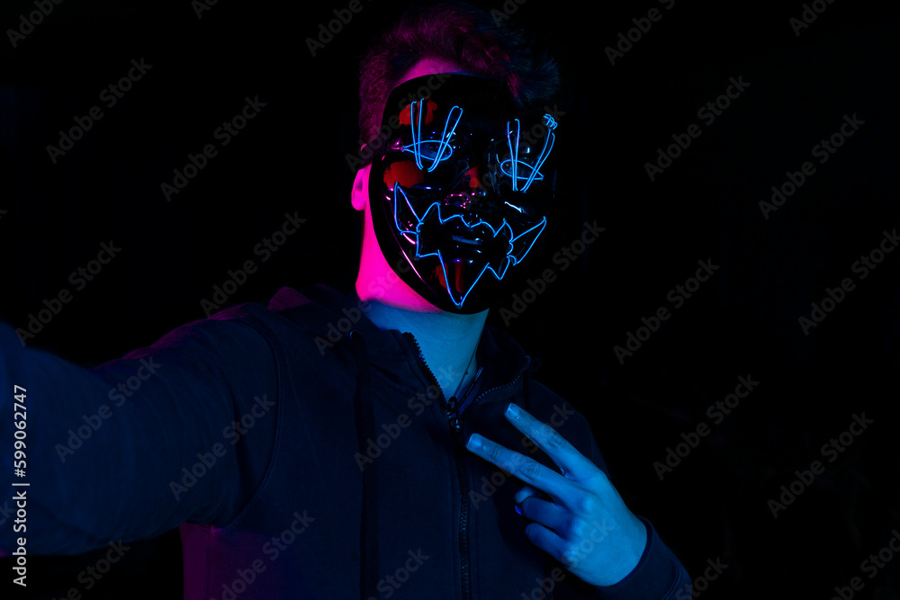 A man wearing a white mask is taking a selfie with his phone on a black background - obrazy, fototapety, plakaty 