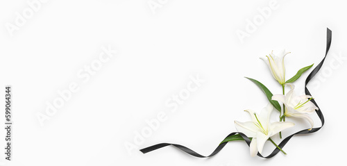 Fototapeta Beautiful lily flowers and black funeral ribbon on white background with space f