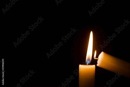 One candle lights another on dark background
