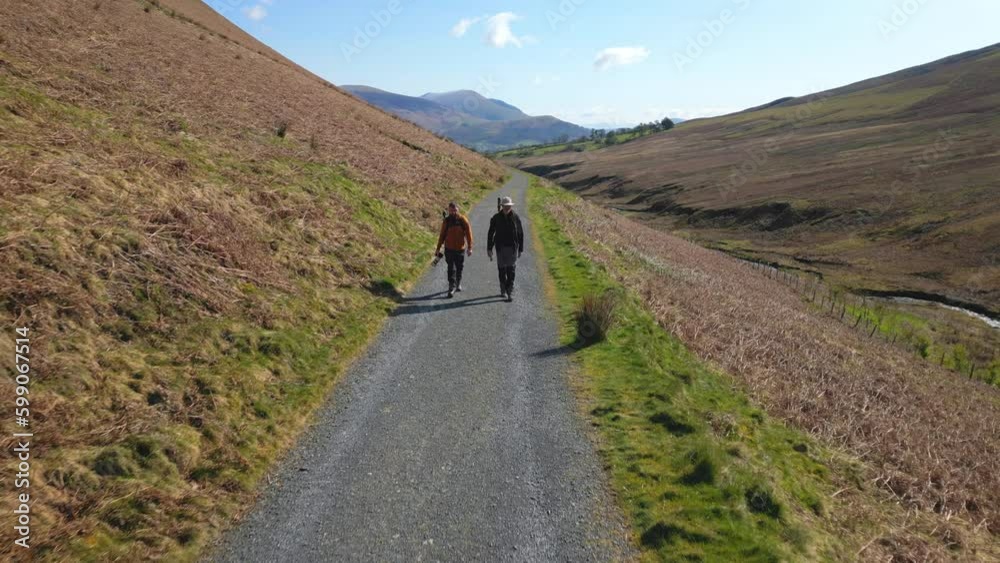 Hikers walking along gravel track towards camera at Coledale Beck in the English Lake District Cumbria Hikers walking along gravel track towards camera at Coledale Beck in the English Lake District Cumbria