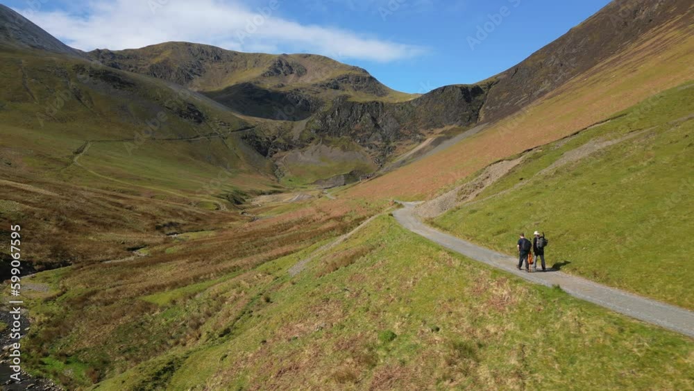 Hikers walking into valley along track on sunny day at Coledale Beck in the English Lake District Cumbria Hikers walking into valley along track on sunny day at Coledale Beck in the English Lake District Cumbria