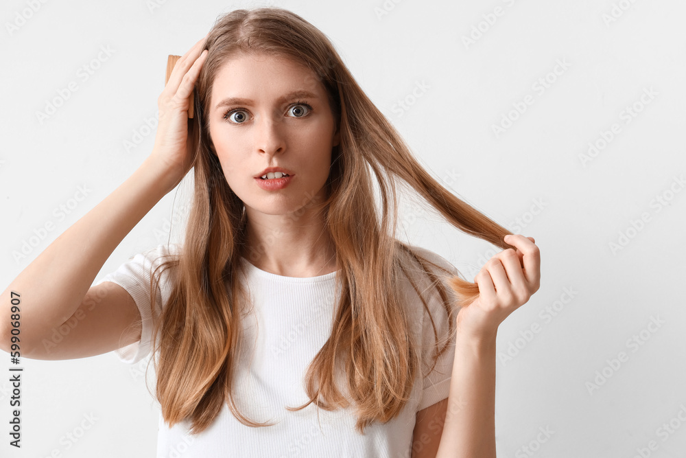 Shocked young woman with hair loss problem and comb on light background Shocked young woman with hair loss problem and comb on light background