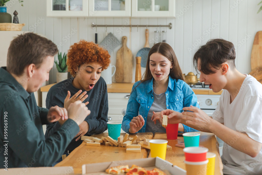 Home party. Friends spending time together playing in board game crash wooden tower at home. Happy diverse group having fun together indoor. Mixed race young buddies best friends enjoying weekend Home party. Friends spending time together playing in board game crash wooden tower at home. Happy diverse group having fun together indoor. Mixed race young buddies best friends enjoying weekend