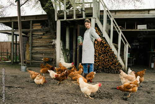 Fotografie an attractive young woman standing near the chicken coop holding a jar with grai