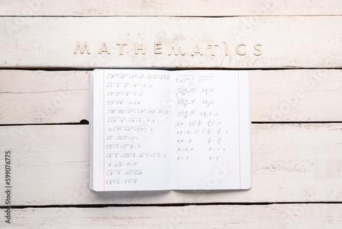 Copybook with formulas and text MATHEMATICS on white wooden background