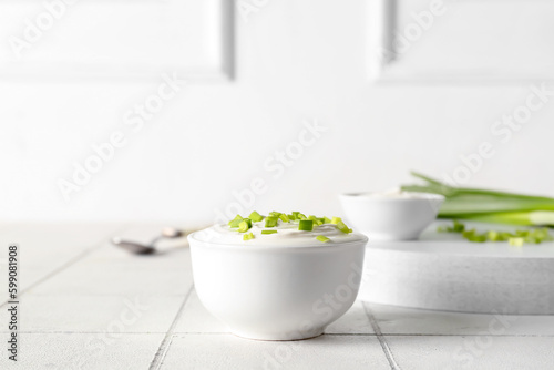 Fototapeta Naklejka Na Ścianę i Meble -  Bowl with sour cream and sliced green onion on white tile table