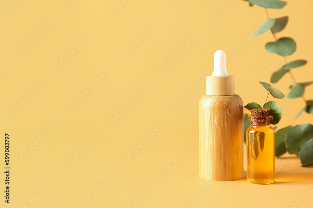 Bottles of cosmetic oil with eucalyptus branches on yellow background