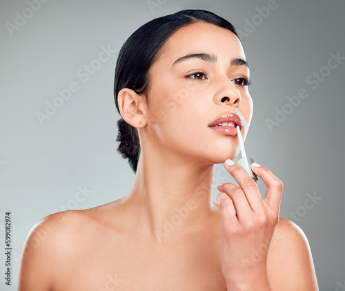 A beautiful young mixed race woman with glowing skin posing against grey copyspace background. Hispanic woman applying lipstick in a studio