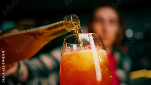 Preparation of Aperol Spritz cocktail bartender pouring prosecco into a glass with ice at the bar close-up
