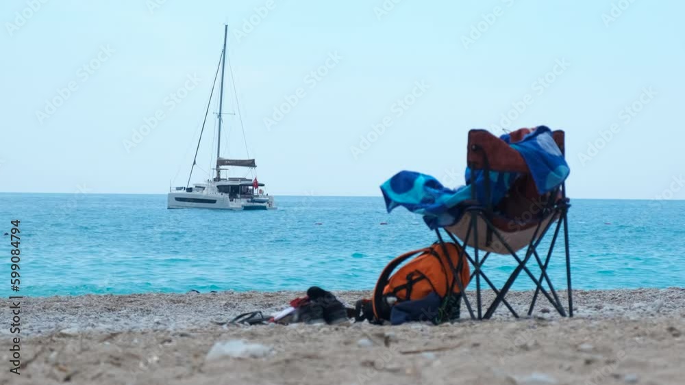 Trip equipment on luxury beach. A view of luxury beach with trip chair and clothes against sea with sailing yacht. A concept of summer relaxation and sea traveling. Generative AI Trip equipment on luxury beach. A view of luxury beach with trip chair and clothes against sea with sailing yacht. A concept of summer relaxation and sea traveling. Generative AI