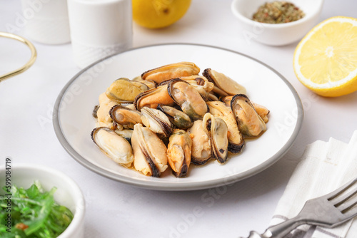 Plate with pickled mussels and bowl of seaweed salad on white background