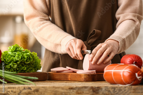 Woman cutting boiled sausage at table in kitchen