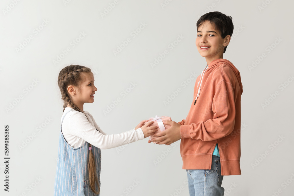 Little boy greeting his sister with gift on light background. Children's Day celebration Little boy greeting his sister with gift on light background. Children's Day celebration