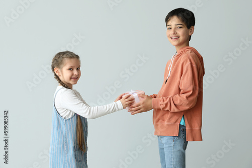 Little boy greeting his sister with gift on light background. Children's Day celebration