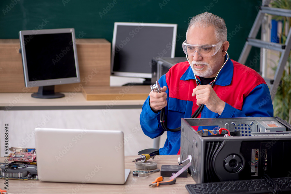 Old repairman repairing computers in the classroom Old repairman repairing computers in the classroom