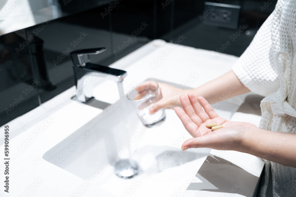 Pills on one hand and another hand hold glass for get water from basin faucet in bathroom, take pills concept. Pills on one hand and another hand hold glass for get water from basin faucet in bathroom, take pills concept.