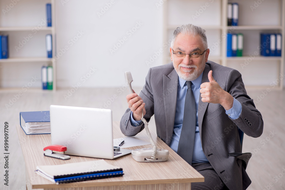 Old male employee speaking by phone at workplace Old male employee speaking by phone at workplace