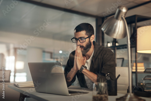 Please work, please work. a young businessman looking anxious while using a laptop during a late night at work.