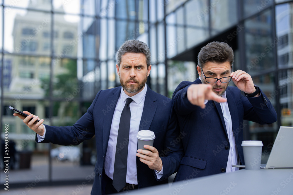 Expression face of emotional business man. Serious businessman pointing finger on you. Portrait of businessman in suit outdoor. The partnership between the two business men. Expression face of emotional business man. Serious businessman pointing finger on you. Portrait of businessman in suit outdoor. The partnership between the two business men.