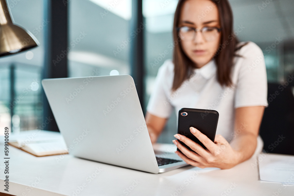 Keeping up with her business connections. a young businesswoman using a cellphone and laptop in an office. Keeping up with her business connections. a young businesswoman using a cellphone and laptop in an office.