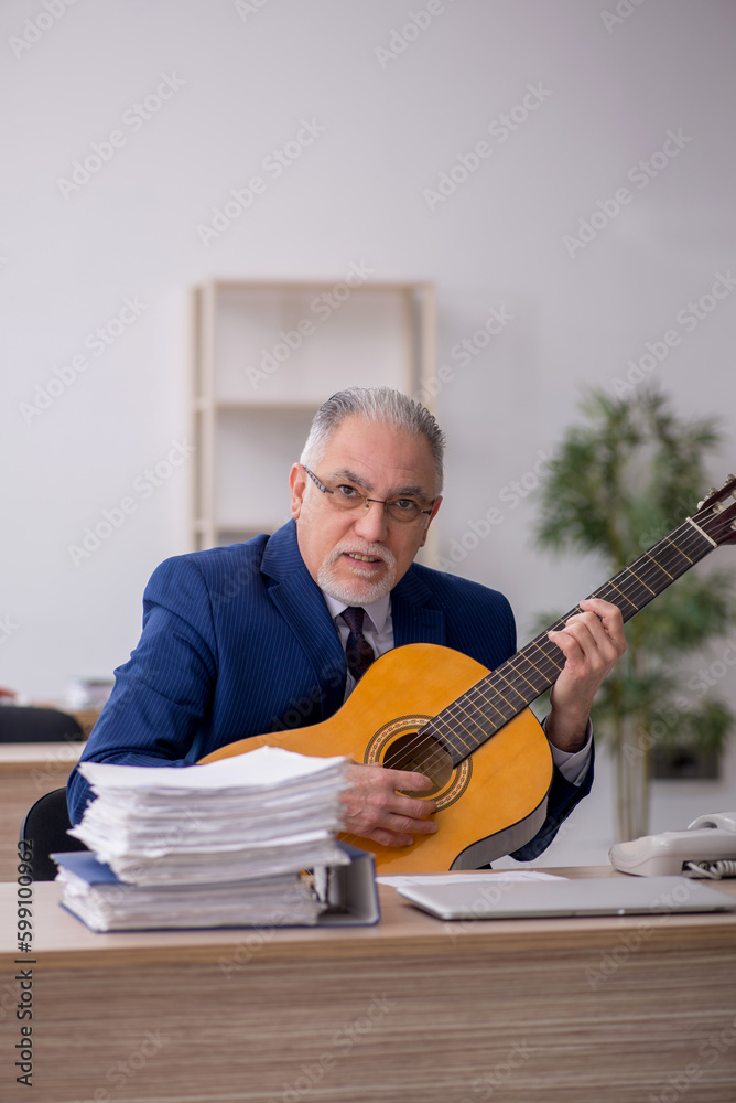 Obraz premium Old male employee playing guitar at workplace
