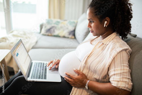 Young pregnant woman using a laptop at home on the couch