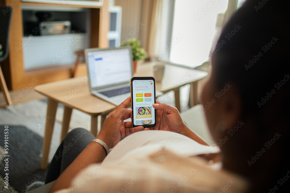 Young pregnant latina woman using a diet app on her smart phone while sitting on a couch in the living room of her home Young pregnant latina woman using a diet app on her smart phone while sitting on a couch in the living room of her home