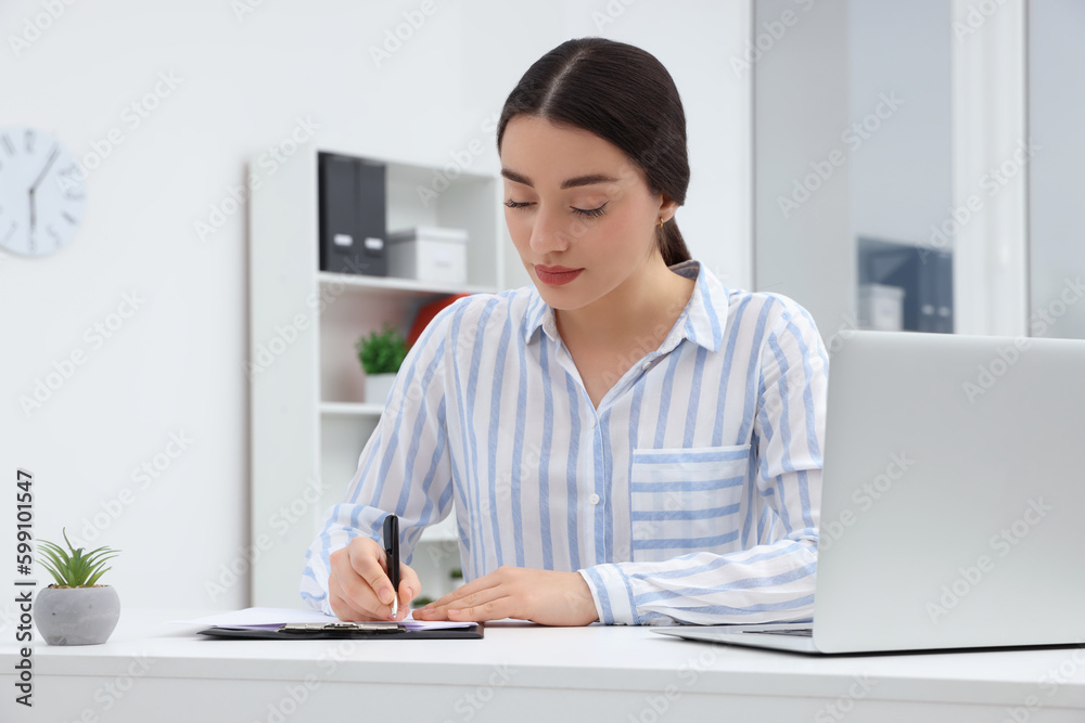 Young female intern working with laptop at table in office Young female intern working with laptop at table in office