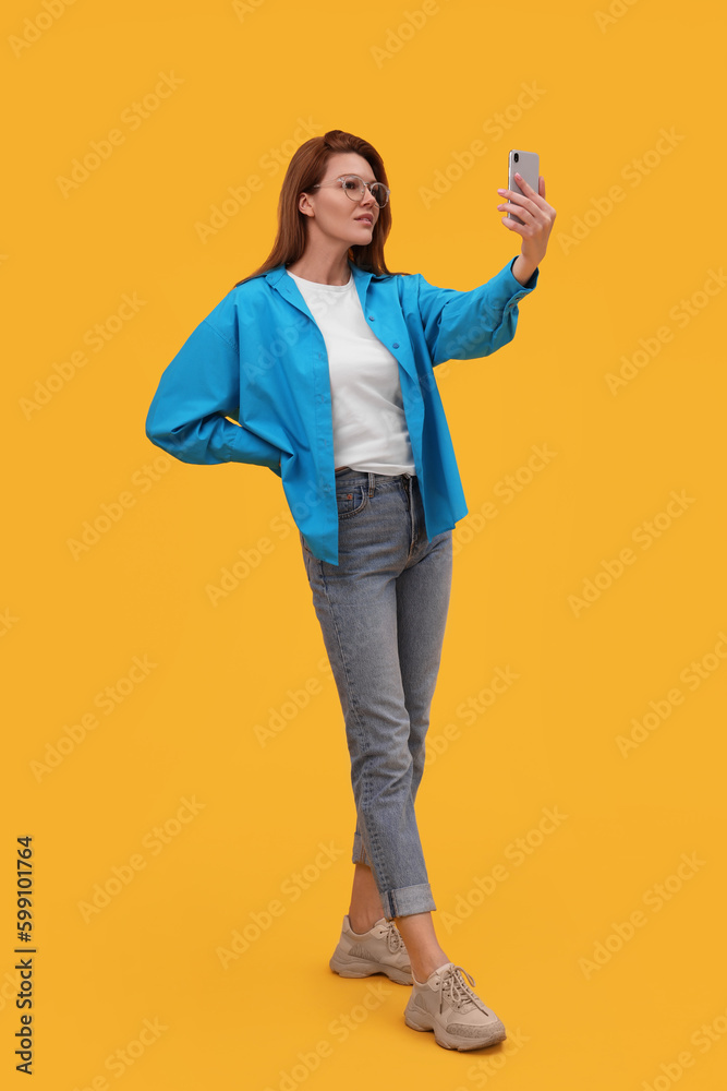 Beautiful woman in eyeglasses taking selfie on orange background Beautiful woman in eyeglasses taking selfie on orange background