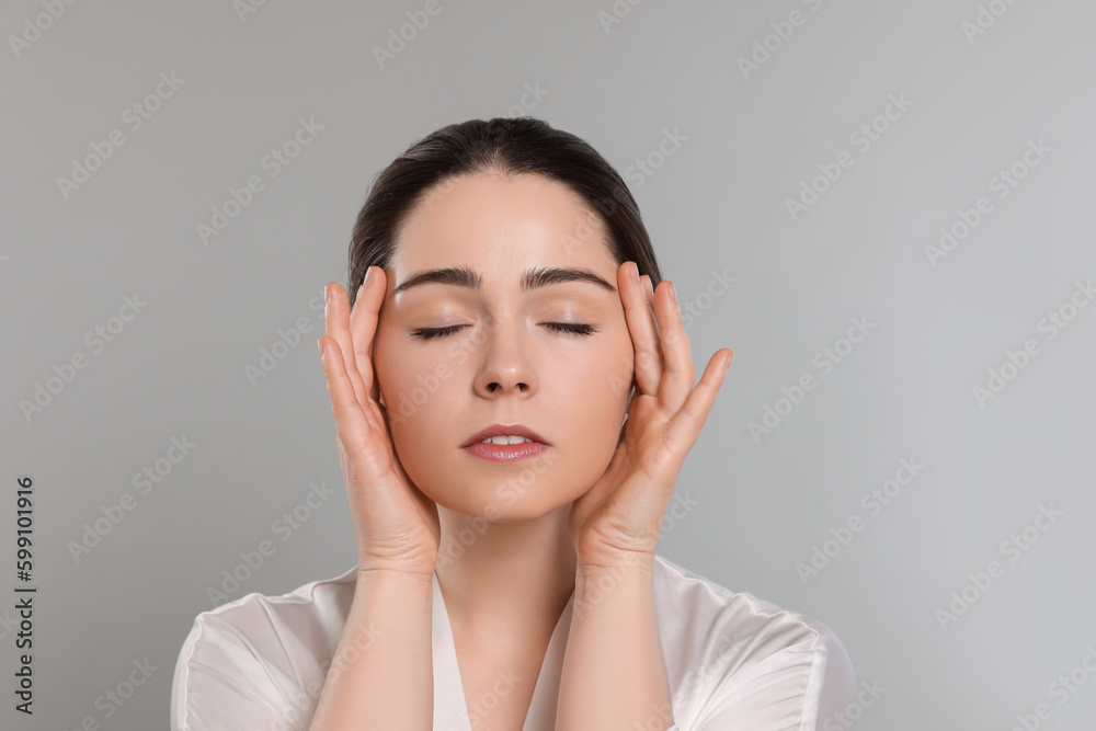 Young woman massaging her face on grey background Young woman massaging her face on grey background