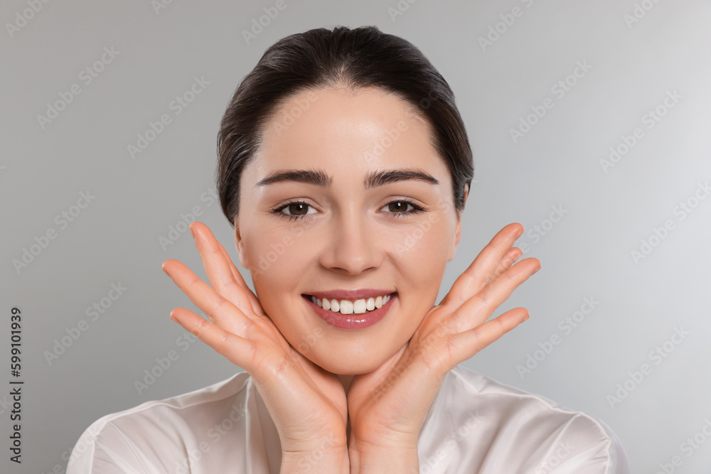Young woman massaging her face on grey background Young woman massaging her face on grey background