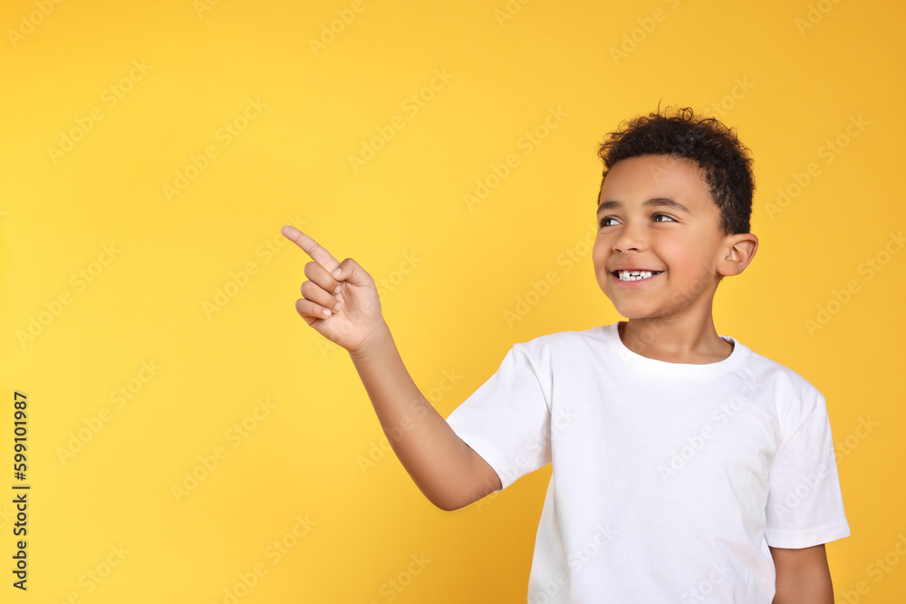 Cute African-American boy pointing on yellow background. Space for text Cute African-American boy pointing on yellow background. Space for text