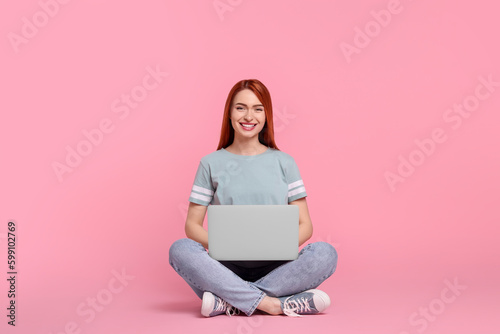 Smiling young woman working with laptop on pink background