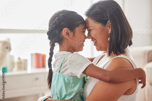 Single mother holding her cute little daughter and looking sweet and happy while sitting on the lounge floor at home