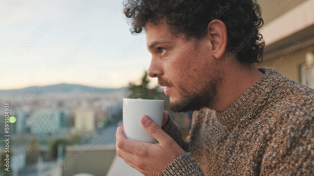 Peaceful guy looks at the city from the balcony and drinks coffee, enjoys the beautiful view Peaceful guy looks at the city from the balcony and drinks coffee, enjoys the beautiful view