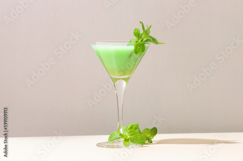 Grasshopper green alcoholic cocktail drink with mint liqueur, cream, ice and fresh mint. Beige background, hard light, shadow pattern, copy space