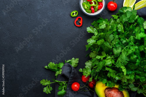 Fresh cilantro or coriander, chili and jalapeno peppers, avocado, lime and cherry tomatoes - ingredients for Mexican spicy cuisine. Black kitchen table background, top view