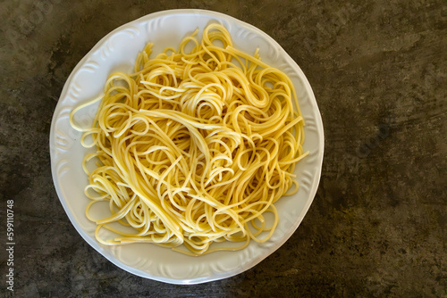 A serving of cooked spaghetti on a white plate on a rustic cement countertop.