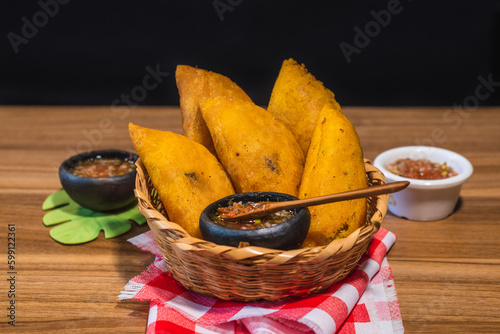 Colombian empanadas. Table with traditional Colombian food, wicker basket with empanada con aji, on a wooden table. black background. photo