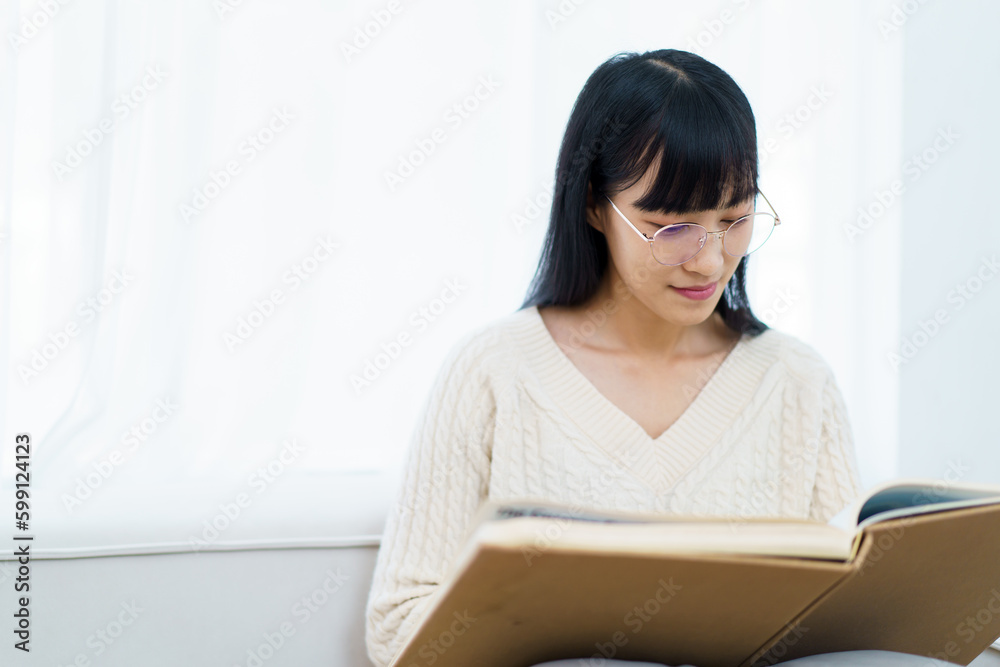 Happy - cheerful Asian young woman with eye glasses sitting on the sofa in living room and reading a book alone. Happy - cheerful Asian young woman with eye glasses sitting on the sofa in living room and reading a book alone.