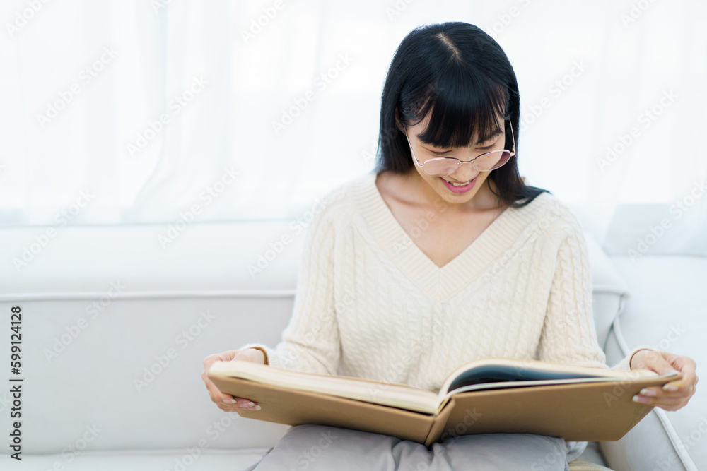 Happy - cheerful Asian young woman with eye glasses sitting on the sofa in living room and reading a book alone. Happy - cheerful Asian young woman with eye glasses sitting on the sofa in living room and reading a book alone.