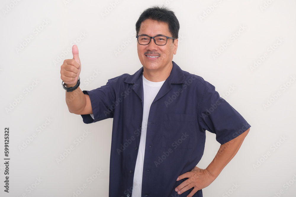 A smiling middle-aged man wearing glasses showing his thumb, one hand on his hip A smiling middle-aged man wearing glasses showing his thumb, one hand on his hip