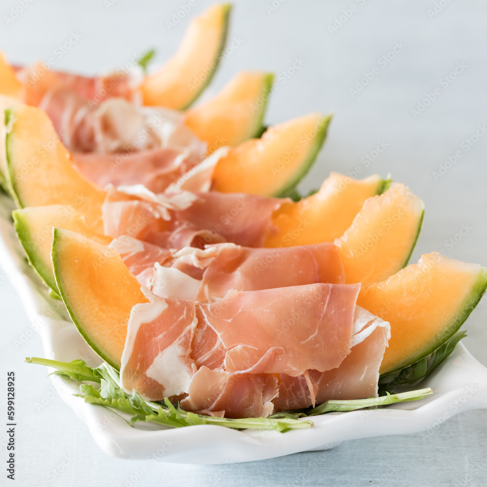 Cantaloupe wedges wrapped in prosciutto on a bed of arugula leaves. Cantaloupe wedges wrapped in prosciutto on a bed of arugula leaves.