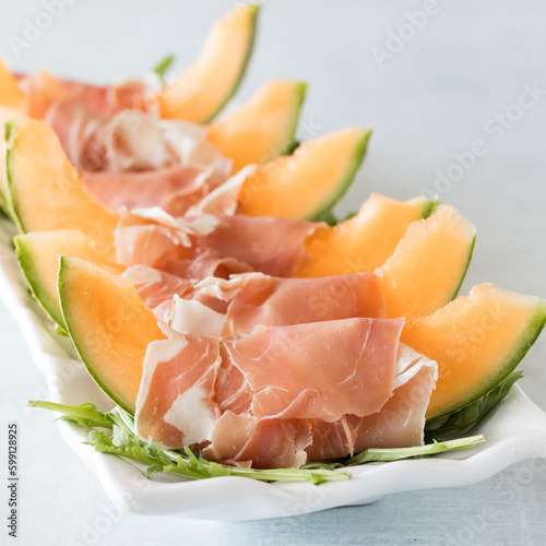 Cantaloupe wedges wrapped in prosciutto on a bed of arugula leaves.