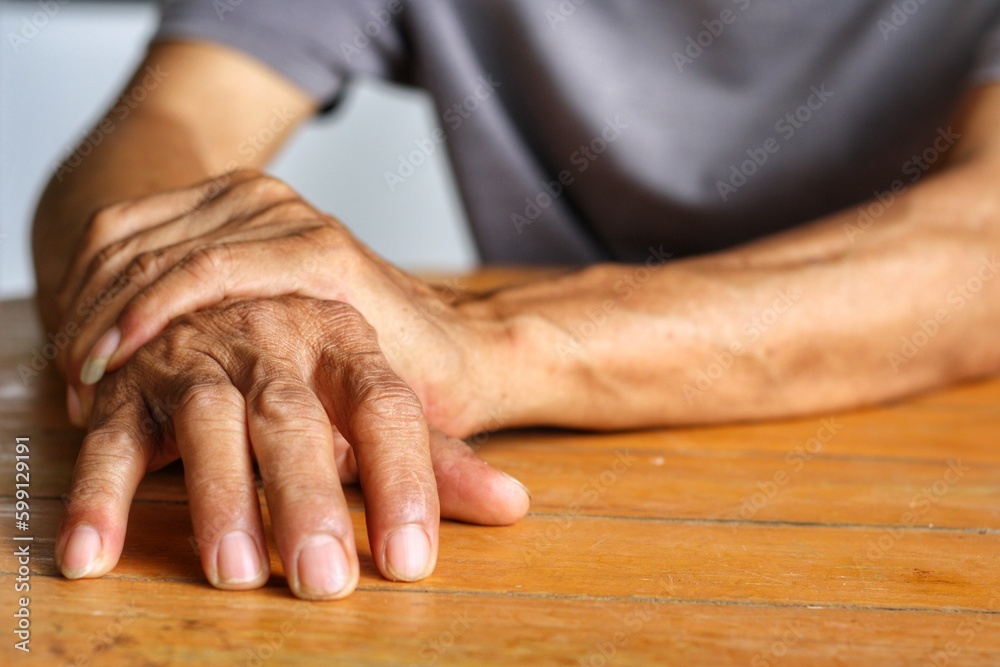 Elderly man is holding his hand and putting on the table because Parkinson's disease.Tremor is most symptom and make a trouble for doing activities such as eat or drink.Health care or elderly concept. Elderly man is holding his hand and putting on the table because Parkinson's disease.Tremor is most symptom and make a trouble for doing activities such as eat or drink.Health care or elderly concept.