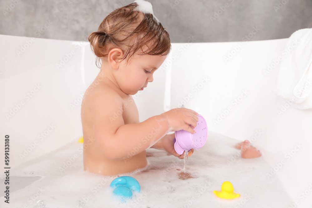 Cute little girl taking bubble bath with toys indoors Cute little girl taking bubble bath with toys indoors