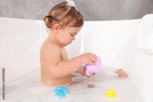 Cute little girl taking bubble bath with toys indoors